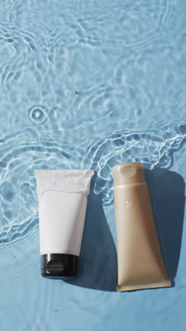 Vertical-video-of-beauty-product-tubes-in-water-with-copy-space-on-blue-background