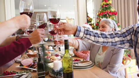 Felices-Y-Diversos-Amigos-Mayores-Haciendo-Un-Brindis-Con-Vino-En-La-Mesa-De-Comedor-Navideña,-Cámara-Lenta