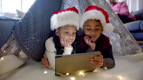 Afroamerikanischer-Bruder-Und-Schwester-In-Weihnachtsmützen-Mit-Tablet-Im-Deckenzelt,-Zeitlupe