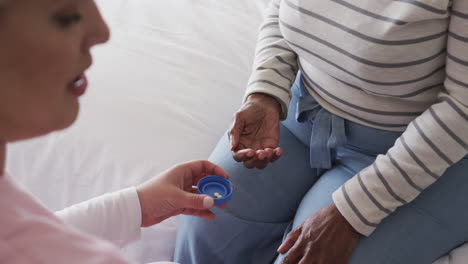 Caucasian-female-nurse-giving-pills-to-senior-african-american-woman,-copy-space,-slow-motion