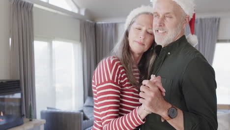 Pareja-Caucásica-De-Mediana-Edad-Con-Sombreros-De-Santa-Bailando-En-Navidad-En-Casa,-Cámara-Lenta