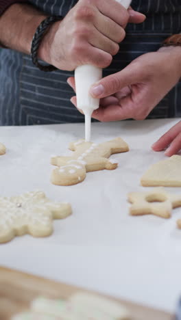 Video-Vertical-De-La-Sección-Media-De-Un-Hombre-Caucásico-Decorando-Galletas-Navideñas,-Cámara-Lenta