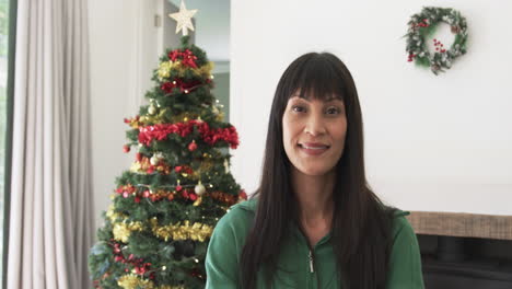 Retrato-De-Una-Mujer-Birracial-Feliz-Sonriendo-Junto-Al-árbol-De-Navidad-En-Casa,-Espacio-Para-Copiar,-Cámara-Lenta