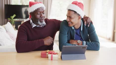 Happy-african-american-father-and-adult-son-in-christmas-hats-having-tablet-video-call,-slow-motion