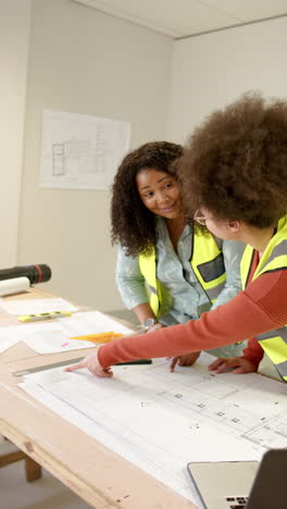 Vertical-video-of-casual-diverse-female-architects-looking-at-plans,-slow-motion,-copy-space