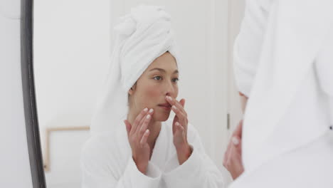 Happy-biracial-woman-touching-her-face-looking-in-mirror-in-bathroom,-slow-motion