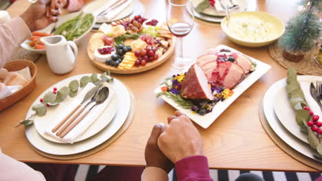 Hands-of-diverse-senior-friends-holding-hands-to-say-grace-before-christmas-dinner,-slow-motion