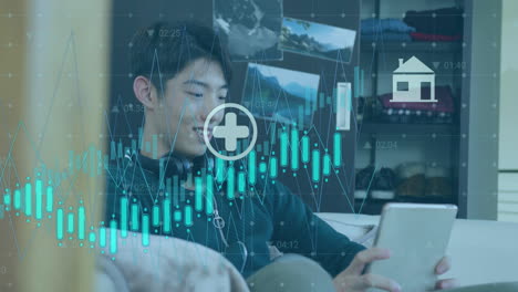 Animation-Mehrerer-Diagramme-Mit-Symbolen-über-Einem-Asiatischen-Jungen,-Der-Auf-Einem-Digitalen-Tablet-Scrollt