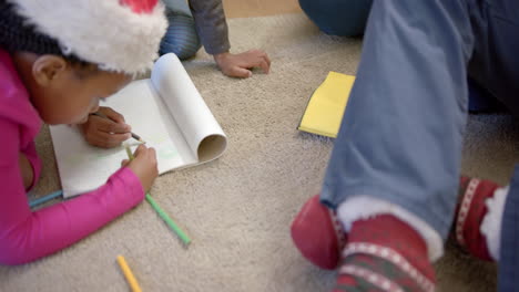 African-american-brother-and-sister-in-christmas-hats-drawing-on-floor-in-living-room,-slow-motion