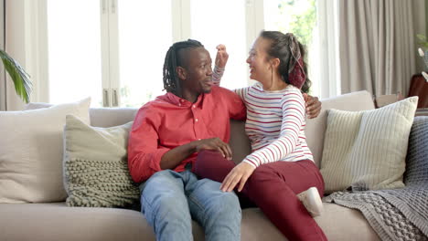 Retrato-De-Una-Feliz-Pareja-Diversa-Sentada-En-El-Sofá-Hablando-En-Una-Soleada-Sala-De-Estar,-Cámara-Lenta