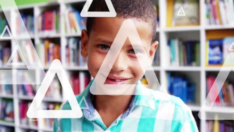 Animation-of-triangles-over-close-up-of-smiling-biracial-boy-standing-in-library-room