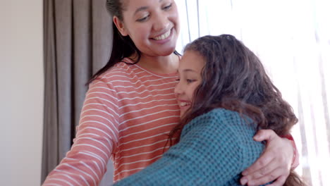 Happy-biracial-mother-and-daughter-dancing-and-embracing-in-sunny-bedroom