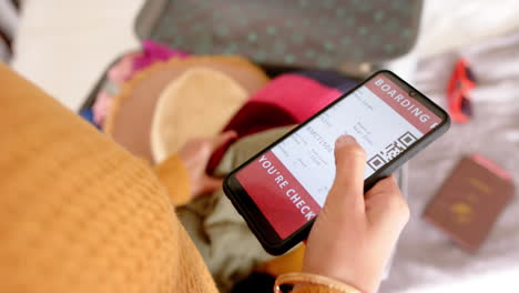 Mid-section-of-caucasian-woman-with-smartphone-and-packing-suitcase-at-home,-copy-space,-slow-motion