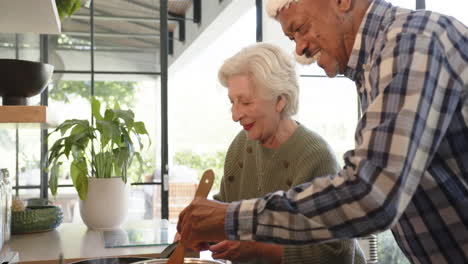 Feliz-Y-Diversa-Pareja-De-Ancianos-En-La-Cocina-Preparando-Comida-De-Celebración-Navideña,-Cámara-Lenta