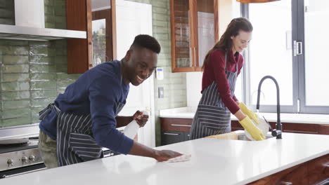 Feliz-Pareja-Diversa-Lavando-Platos-Y-Limpiando-La-Parte-Superior-De-La-Cocina,-Cámara-Lenta