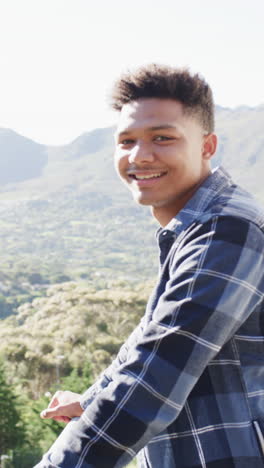 Vertical-video-portrait-of-happy-african-american-man-on-sunny-balcony-in-countryside,-slow-motion