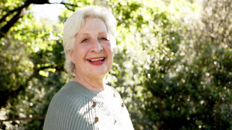 Feliz-Mujer-Caucásica-Mayor-Con-Pelo-Blanco-Sonriendo-En-Un-Jardín-Soleado,-Espacio-Para-Copiar,-Cámara-Lenta