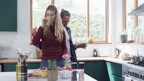 Happy-diverse-couple-preparing-dinner-and-drinking-smoothie-in-kitchen-at-home,-in-slow-motion