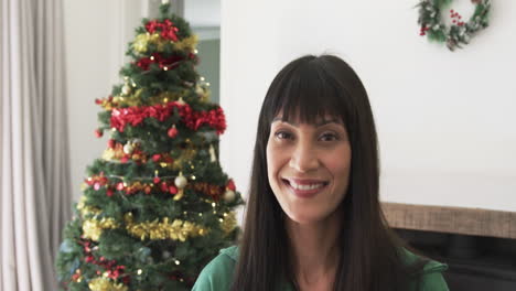 Portrait-of-happy-biracial-woman-smiling-by-christmas-tree-at-home,-copy-space,-slow-motion