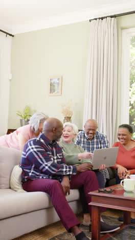 Vertical-video-of-happy-diverse-senior-friends-using-laptop-in-living-room,-copy-space,-slow-motion