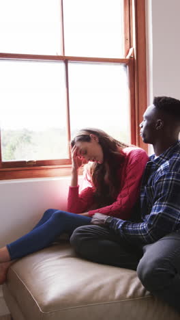 Sad-diverse-couple-embracing-and-sitting-by-window-at-home,-slow-motion,-copy-space
