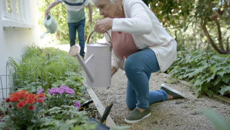 Pareja-Caucásica-Mayor-Regando-Plantas-En-Un-Jardín-Soleado,-Cámara-Lenta