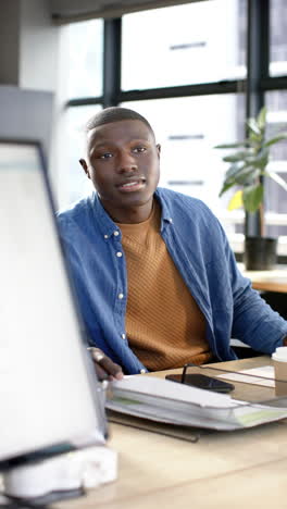 Video-Vertical-De-Un-Hombre-De-Negocios-Afroamericano-Trabajando-En-La-Oficina,-Cámara-Lenta,-Espacio-Para-Copiar