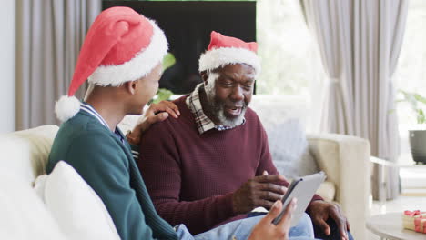 Happy-african-american-father-and-adult-son-in-christmas-hats-having-tablet-video-call,-slow-motion