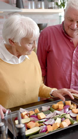 Vertical-video-of-senior-caucasian-couple-cooking-dinner-in-kitchen-at-home,-slow-motion