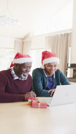 Vertikales-Video-Eines-Afroamerikanischen-Vaters-Und-Sohns-Bei-Einem-Weihnachts-Videoanruf-Mit-Dem-Laptop,-Zeitlupe