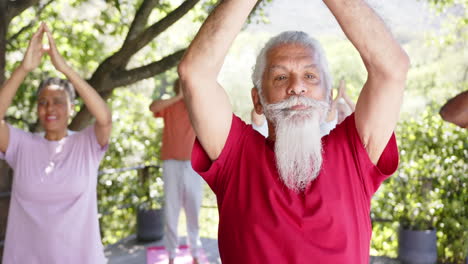 Focused-diverse-senior-male-instructor-and-friends-practicing-yoga-in-sunny-nature,-slow-motion