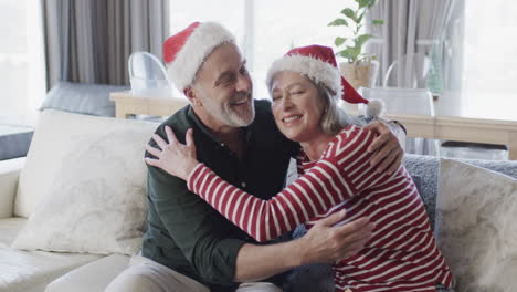 Pareja-Caucásica-De-Mediana-Edad-Con-Sombreros-De-Santa-Abrazándose-En-Navidad-En-Casa,-Cámara-Lenta