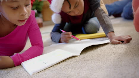 African-american-brother-and-sister-in-christmas-hats-drawing-on-floor-in-living-room,-slow-motion