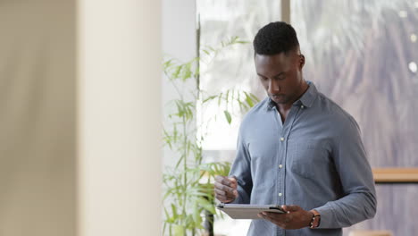 Casual-african-american-businessman-using-tablet-office,-slow-motion-with-copy-space