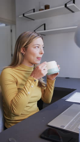 Video-Vertical-Del-Retrato-De-Una-Mujer-Birracial-Feliz-Tomando-Café-En-El-Escritorio-De-Casa,-Cámara-Lenta