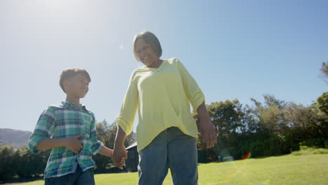 Happy-biracial-grandmother-and-grandson-walking-in-sunny-garden,-slow-motion