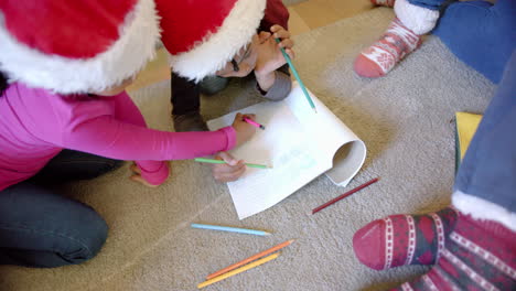 African-american-brother-and-sister-in-christmas-hats-drawing-on-floor-in-living-room,-slow-motion