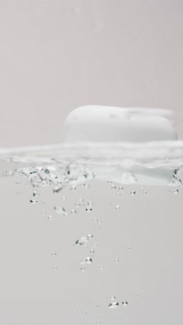 Vertical-video-of-beauty-product-tub-falling-in-water-with-copy-space-on-white-background