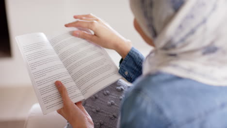 Feliz-Mujer-Birracial-En-Hijab-Leyendo-Un-Libro-En-Un-Sofá-En-Casa-Con-Espacio-Para-Copiar,-Cámara-Lenta