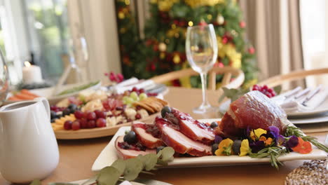 Food-on-dining-table-set-for-christmas-celebration-meal-with-tree-in-background,-slow-motion