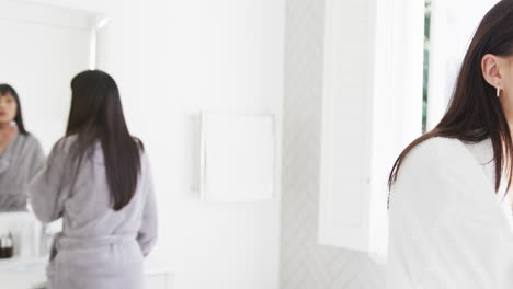 Happy-biracial-mother-and-adult-daughter-cleansing-faces-and-talking-in-sunny-bathroom,-slow-motion