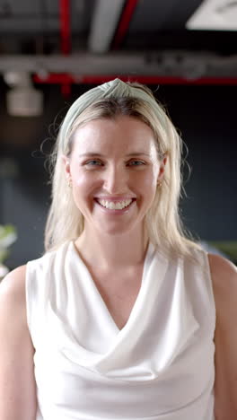 Vertical-video-of-portrait-of-smiling-caucasian-businesswoman-in-office-with-copy-space