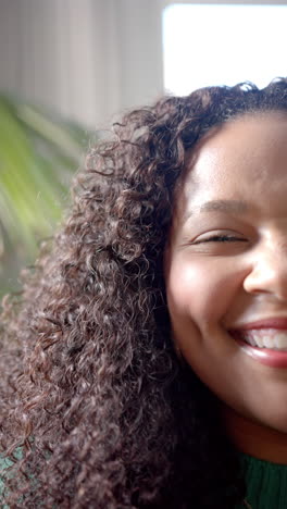 Vertikales-Video-Halbporträt-Einer-Glücklichen-Afroamerikanischen-Frau-Mit-Lockigem-Haar,-Die-In-Einem-Sonnigen-Zimmer-Lächelt