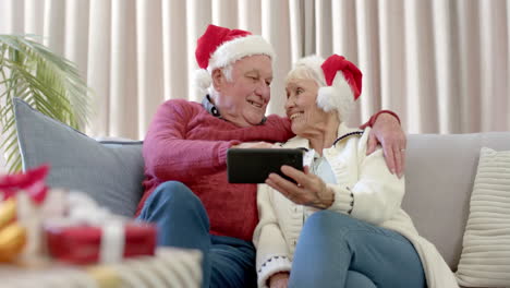 Pareja-Caucásica-Mayor-Con-Sombreros-De-Santa-Usando-Un-Teléfono-Inteligente-Para-Videollamadas-Navideñas,-Cámara-Lenta