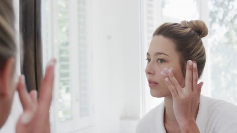 Mujer-Birracial-Aplicando-Crema-Facial-Mirando-El-Espejo-En-El-Baño,-Cámara-Lenta