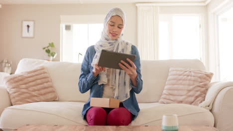 Feliz-Mujer-Birracial-En-Hijab-Usando-Tableta-En-El-Sofá-En-Casa-Con-Espacio-Para-Copiar,-Cámara-Lenta