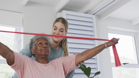 Caucasian-nurse-with-senior-woman-exercising-with-rubber-band,-copy-space,-slow-motion