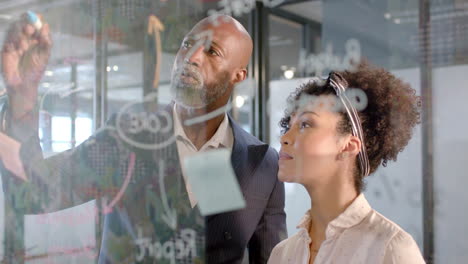 African-american-businessman-writing-on-glass-wall-in-office-with-copy-space