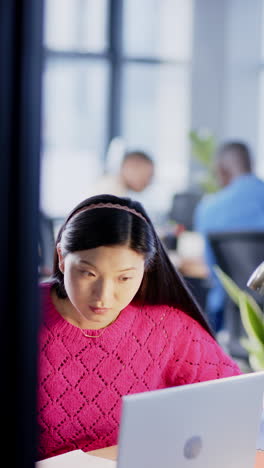 Vertical-video-of-asian-businesswoman-using-computer-in-office,-slow-motion,-copy-space