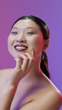 Vertical-video-of-asian-woman-with-black-hair-and-make-up-touching-face,-copy-space,-slow-motion